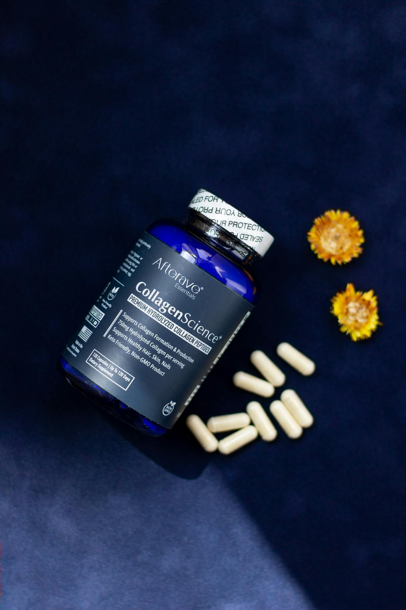 Collagen supplement bottle with capsules and flowers on dark background.
